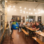 Presenter holding inflatable globe in front of audience at West Sixth Brewery